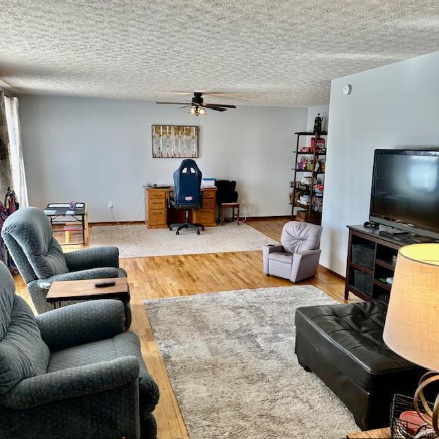 living room with a ceiling fan, a textured ceiling, baseboards, and wood finished floors