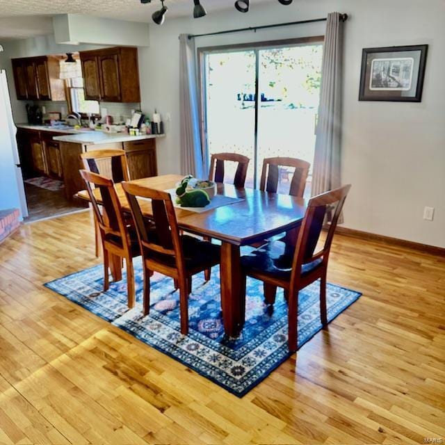 dining area with baseboards, a textured ceiling, and light wood finished floors