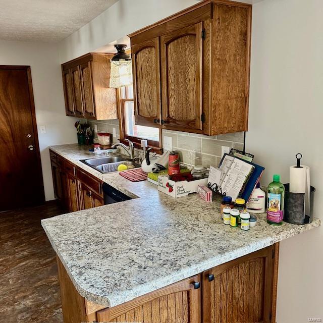 kitchen with brown cabinets, tasteful backsplash, light countertops, a sink, and a peninsula