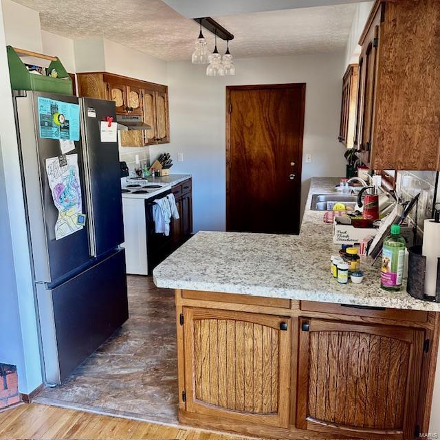 kitchen featuring under cabinet range hood, white electric range, a sink, light countertops, and freestanding refrigerator