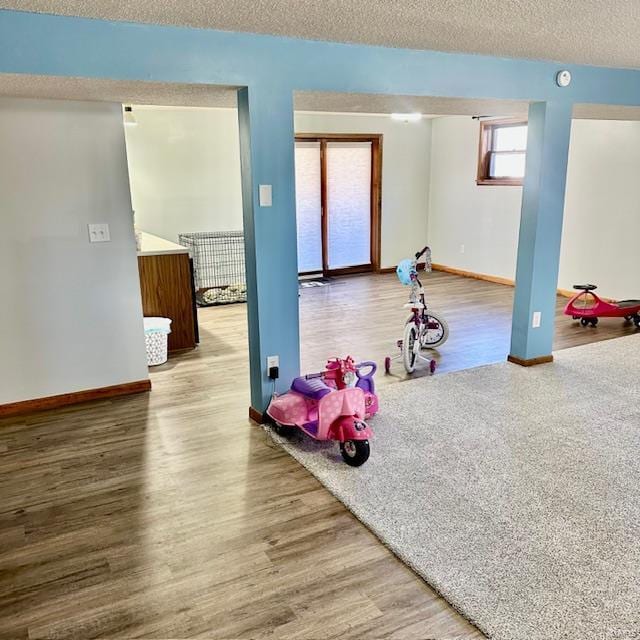 rec room with baseboards, a textured ceiling, and wood finished floors