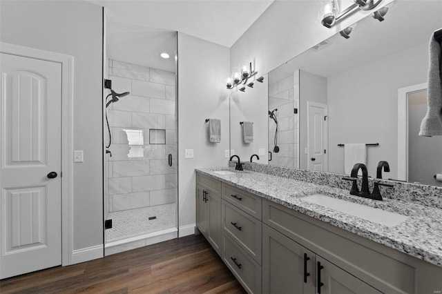 bathroom featuring double vanity, wood finished floors, a stall shower, and a sink