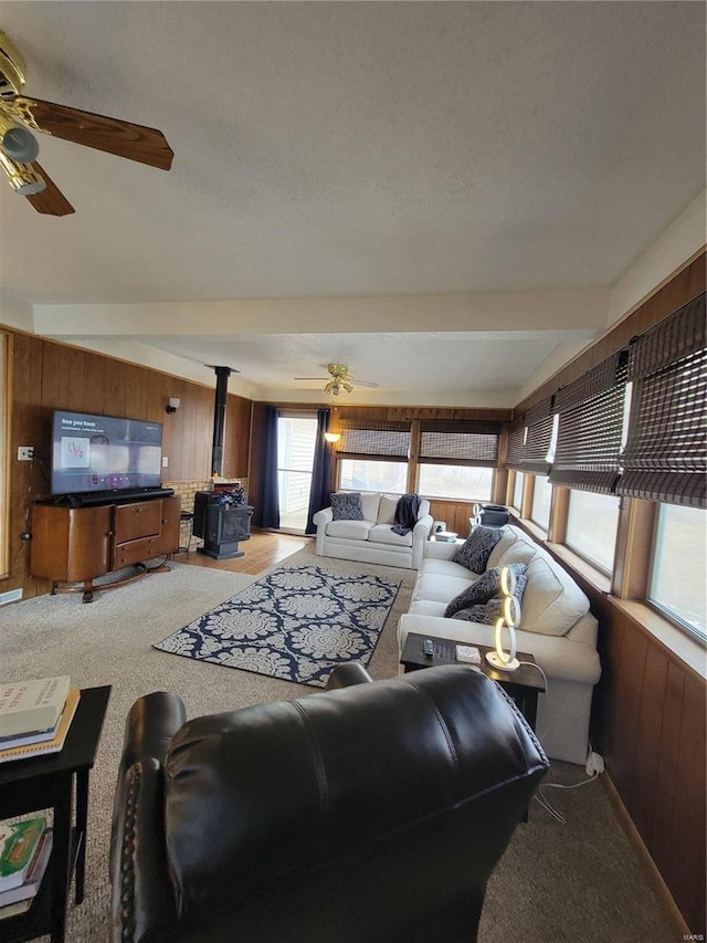 living room with a wood stove, wood walls, a ceiling fan, and light colored carpet