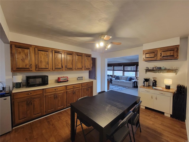 kitchen featuring dark wood-style floors, brown cabinets, light countertops, ceiling fan, and black microwave