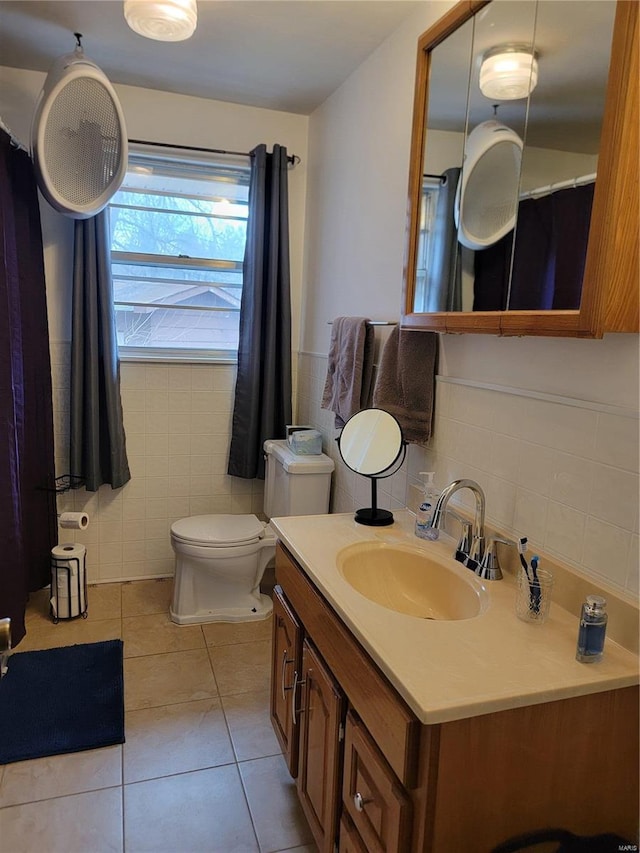 full bath with toilet, a wainscoted wall, tile patterned floors, vanity, and tile walls