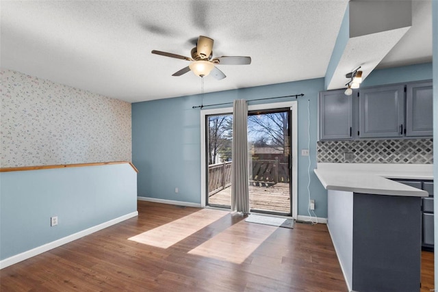 unfurnished dining area with wallpapered walls, baseboards, ceiling fan, dark wood-type flooring, and a textured ceiling