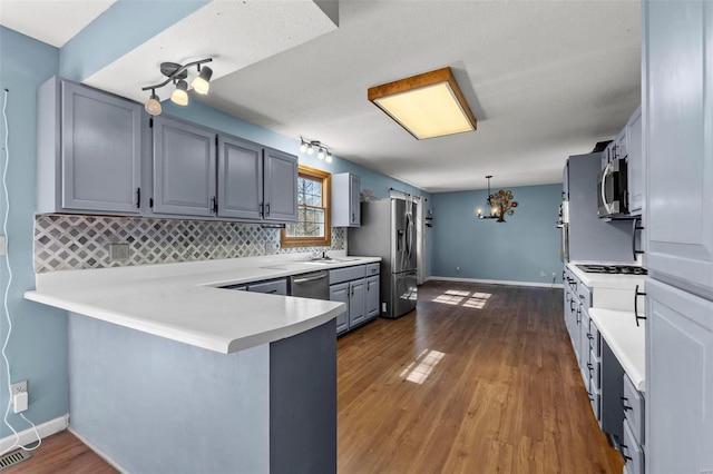 kitchen featuring dark wood-style floors, a peninsula, stainless steel appliances, light countertops, and a sink