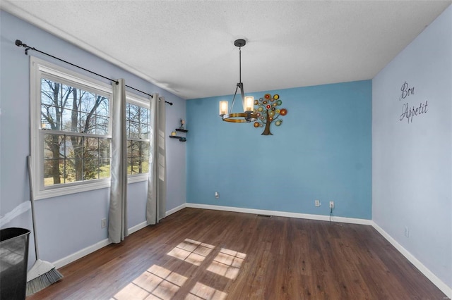 unfurnished dining area featuring a notable chandelier, a textured ceiling, baseboards, and wood finished floors