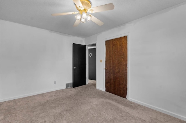 carpeted empty room with baseboards, visible vents, and a ceiling fan