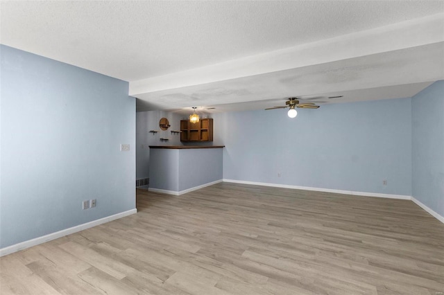 unfurnished living room featuring a ceiling fan, a textured ceiling, baseboards, and wood finished floors