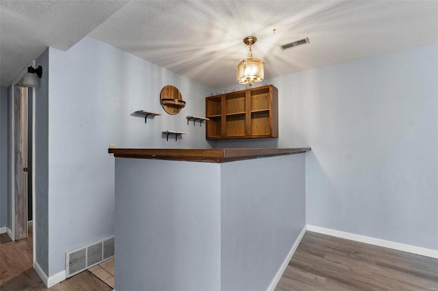 bar featuring a textured ceiling, wood finished floors, visible vents, and baseboards