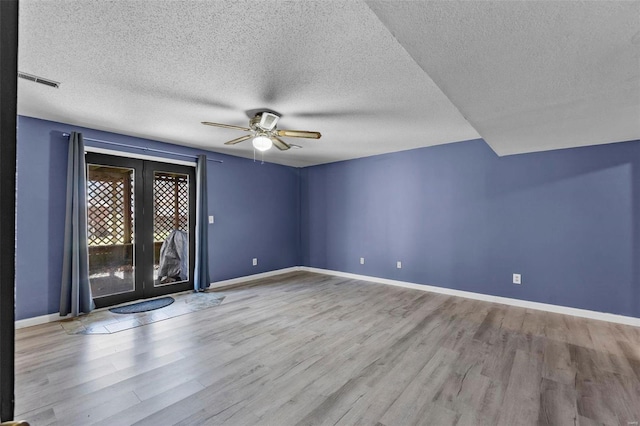 empty room featuring a ceiling fan, visible vents, baseboards, and wood finished floors