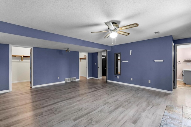 unfurnished living room featuring baseboards, visible vents, a ceiling fan, wood finished floors, and a textured ceiling