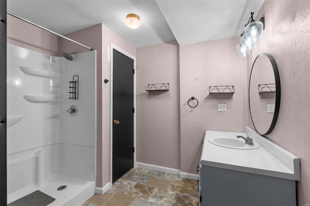 full bathroom featuring stone finish flooring, vanity, baseboards, and walk in shower