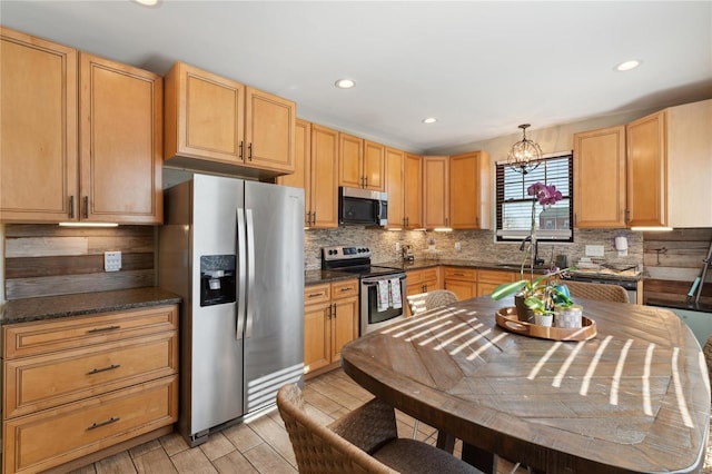 kitchen with wood finish floors, a notable chandelier, dark countertops, tasteful backsplash, and appliances with stainless steel finishes