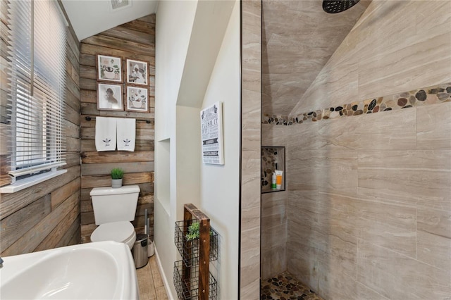 bathroom with a tile shower, toilet, and vaulted ceiling