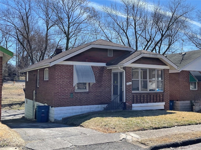 bungalow featuring entry steps, a chimney, a front lawn, and brick siding