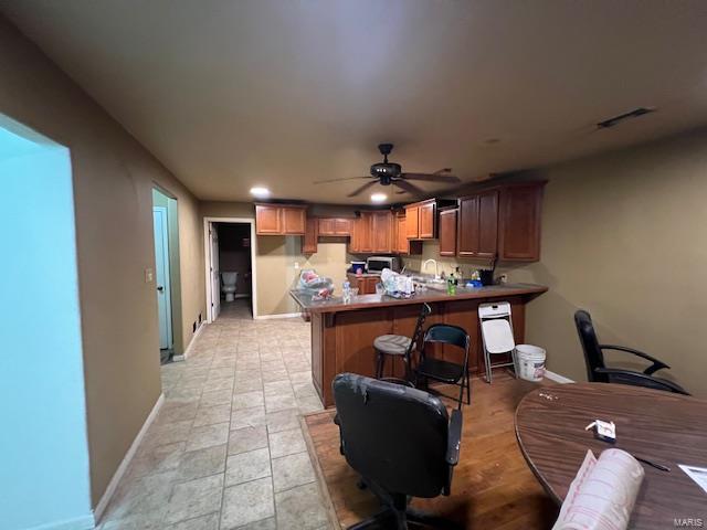 kitchen featuring a breakfast bar area, a peninsula, a ceiling fan, visible vents, and baseboards