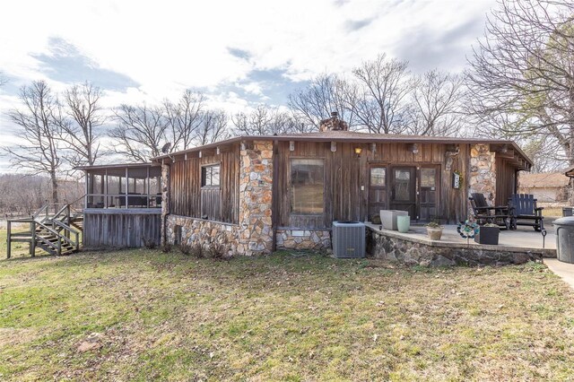 rear view of property featuring a sunroom, stone siding, a chimney, a yard, and central air condition unit