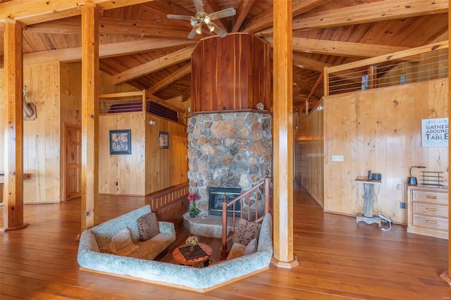 interior space featuring lofted ceiling with beams, wood walls, hardwood / wood-style floors, and a stone fireplace