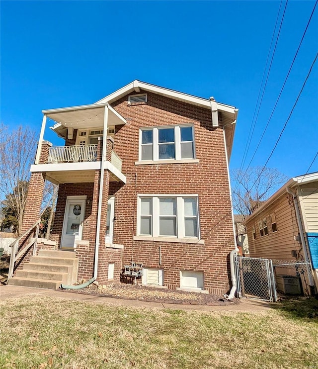 view of front of property featuring a front yard, a balcony, brick siding, and a gate
