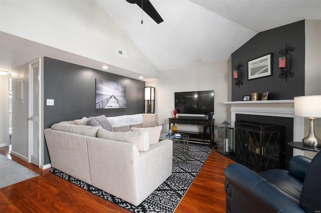 living area with visible vents, a ceiling fan, wood finished floors, vaulted ceiling, and a fireplace