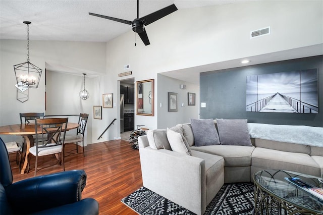 living area featuring high vaulted ceiling, ceiling fan with notable chandelier, visible vents, and wood finished floors