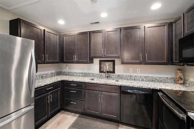 kitchen featuring dark brown cabinetry, visible vents, a sink, and black appliances