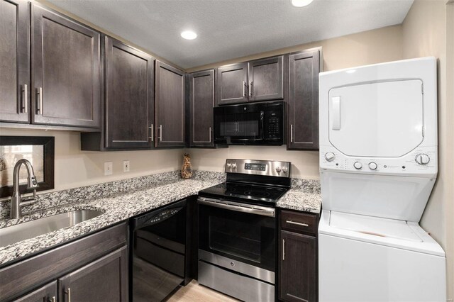 kitchen featuring dark brown cabinetry, black appliances, stacked washer and dryer, and a sink