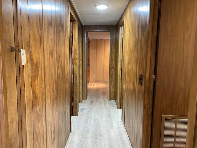 corridor with light wood-style floors, wooden walls, and visible vents