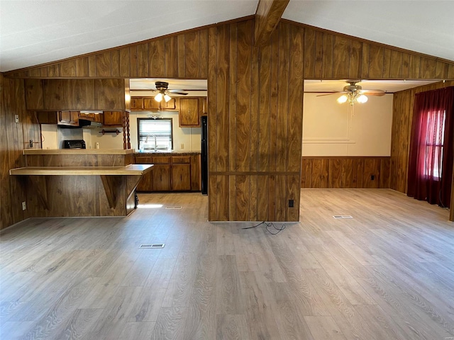 kitchen featuring visible vents, vaulted ceiling, wooden walls, and light wood finished floors