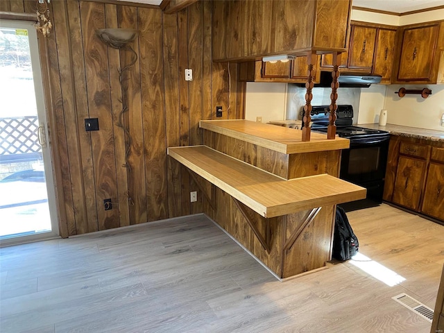 kitchen featuring wooden walls, a peninsula, black range with electric stovetop, visible vents, and light wood-style floors