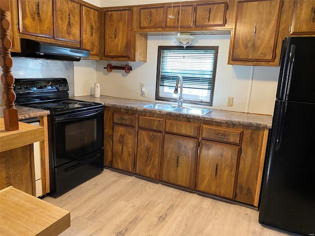 kitchen featuring dark countertops, light wood-style flooring, a sink, under cabinet range hood, and black appliances