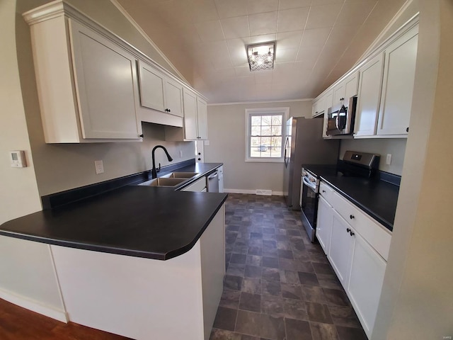 kitchen with dark countertops, a peninsula, stainless steel appliances, white cabinetry, and a sink