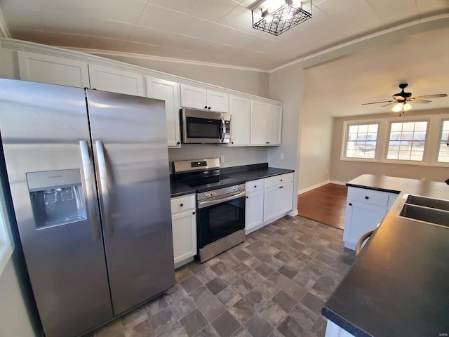 kitchen featuring white cabinets, dark countertops, appliances with stainless steel finishes, ornamental molding, and a sink