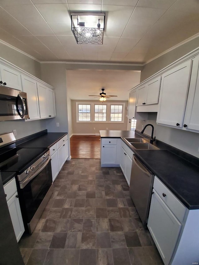 kitchen with white cabinets, dark countertops, a peninsula, stainless steel appliances, and a sink