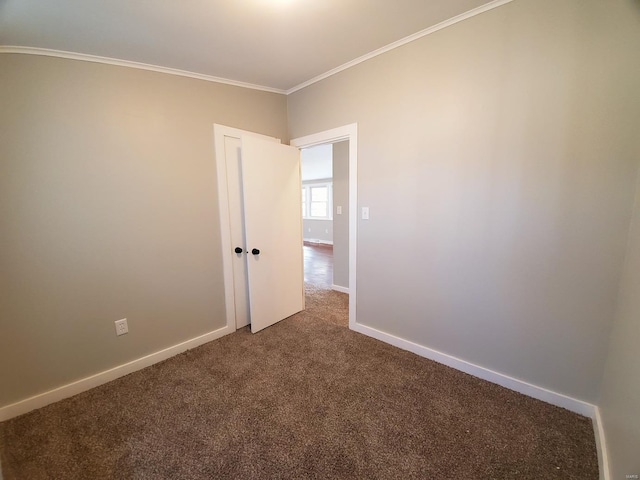 spare room with dark colored carpet, crown molding, and baseboards