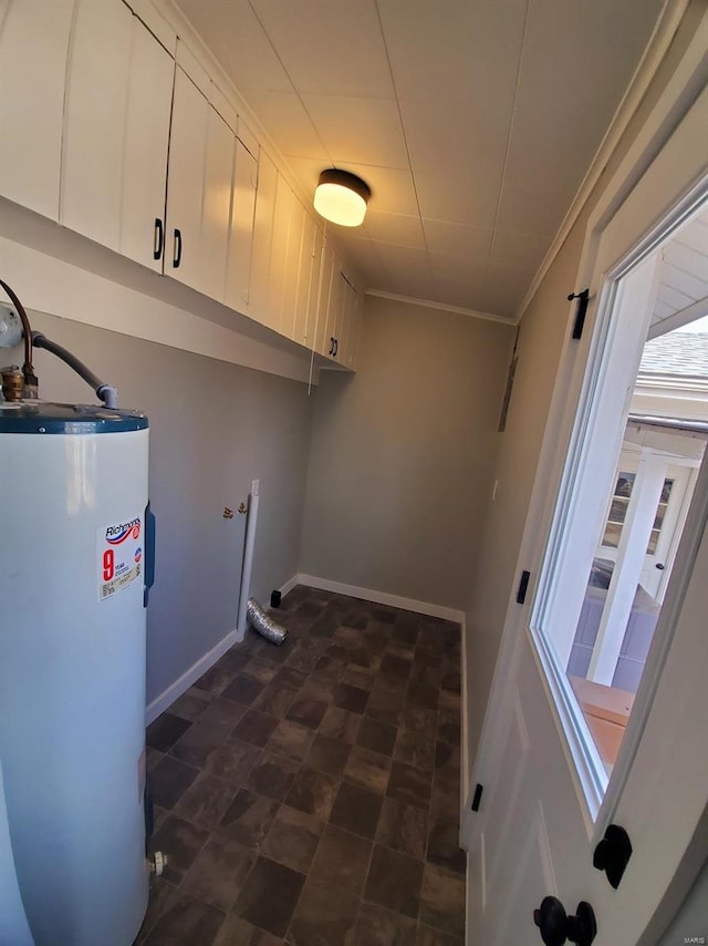 clothes washing area with ornamental molding, gas water heater, cabinet space, and baseboards