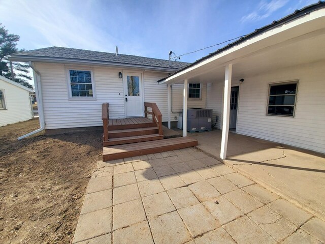 rear view of property featuring cooling unit, a patio area, and roof with shingles