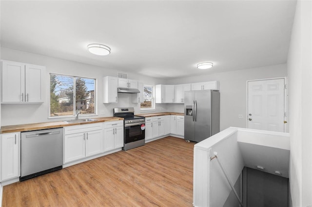 kitchen with butcher block countertops, stainless steel appliances, under cabinet range hood, white cabinetry, and a sink