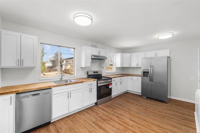 kitchen featuring stainless steel appliances, white cabinets, a sink, butcher block countertops, and under cabinet range hood