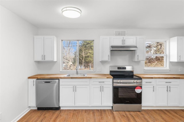 kitchen with white cabinets, butcher block counters, appliances with stainless steel finishes, under cabinet range hood, and a sink