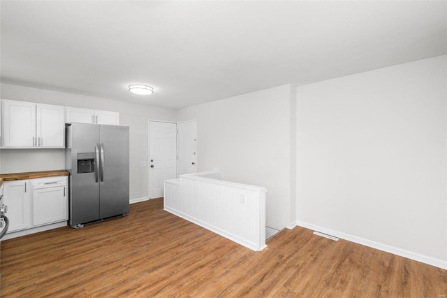 kitchen featuring light wood finished floors, stainless steel fridge, butcher block countertops, and white cabinetry