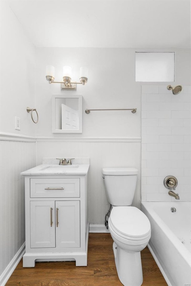 bathroom with toilet, a wainscoted wall, wood finished floors, vanity, and washtub / shower combination