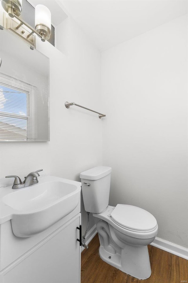 half bath with toilet, baseboards, wood finished floors, and vanity