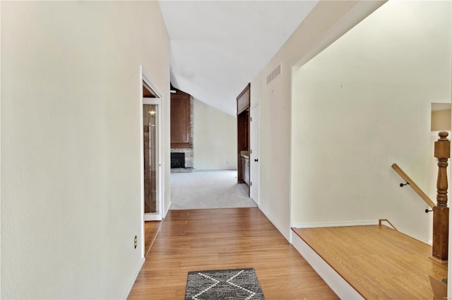 corridor featuring vaulted ceiling, light wood-style flooring, an upstairs landing, and visible vents