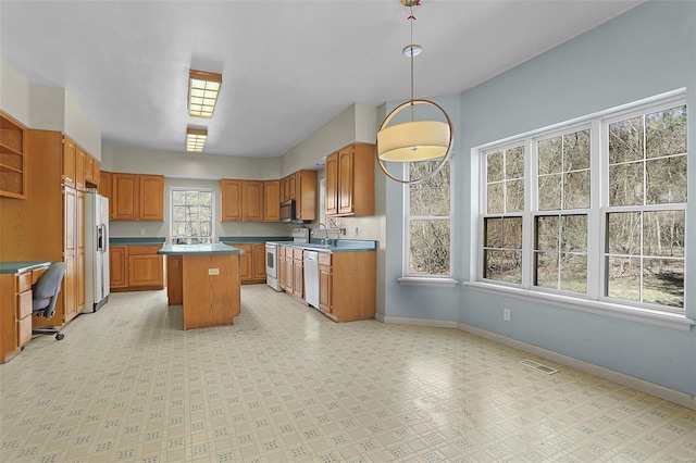 kitchen featuring a kitchen island, white appliances, brown cabinetry, baseboards, and light floors