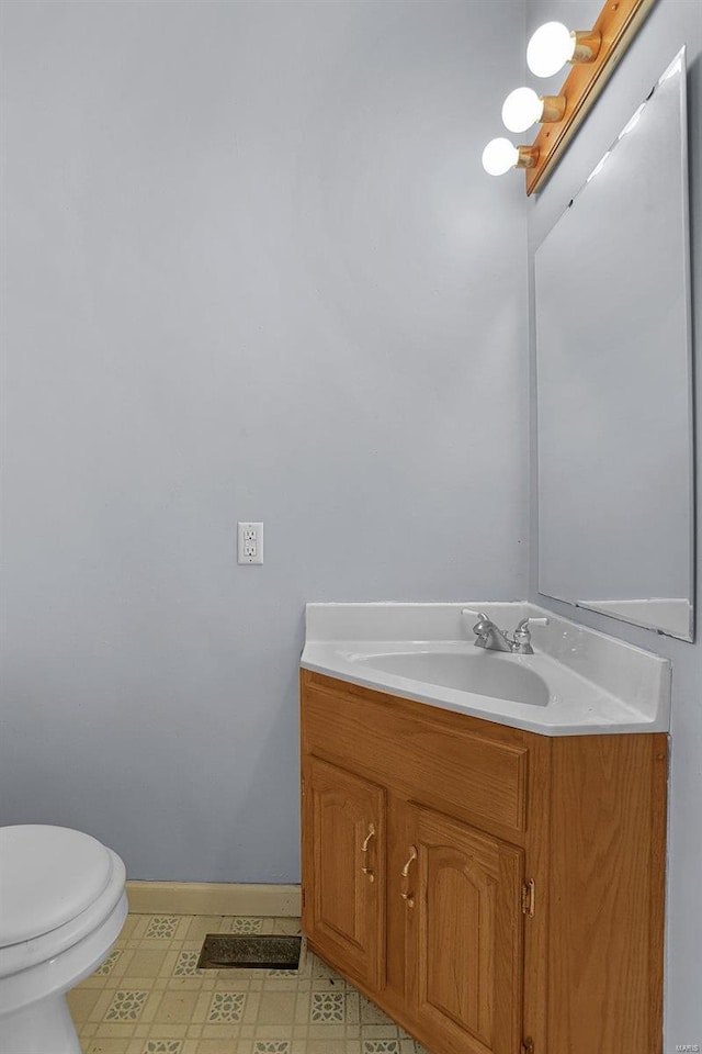 half bath featuring tile patterned floors, toilet, vanity, and baseboards