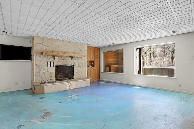 unfurnished living room with baseboards, concrete flooring, and a stone fireplace