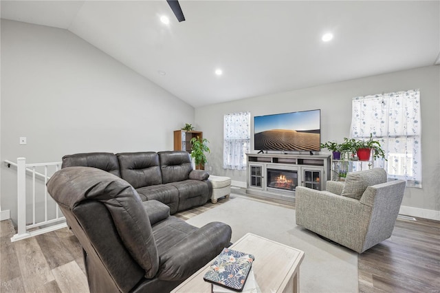 living room with a wealth of natural light, a glass covered fireplace, vaulted ceiling, and wood finished floors